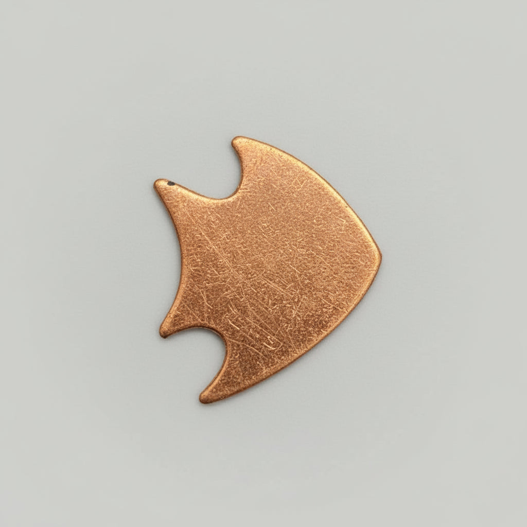 A small, angle fish shaped copper blank placed against a measuring grid background, indicated as a 1-inch size sample.