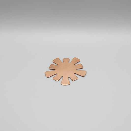 A copper blank in the shape of a flower or star laid on a ruler for measurement.