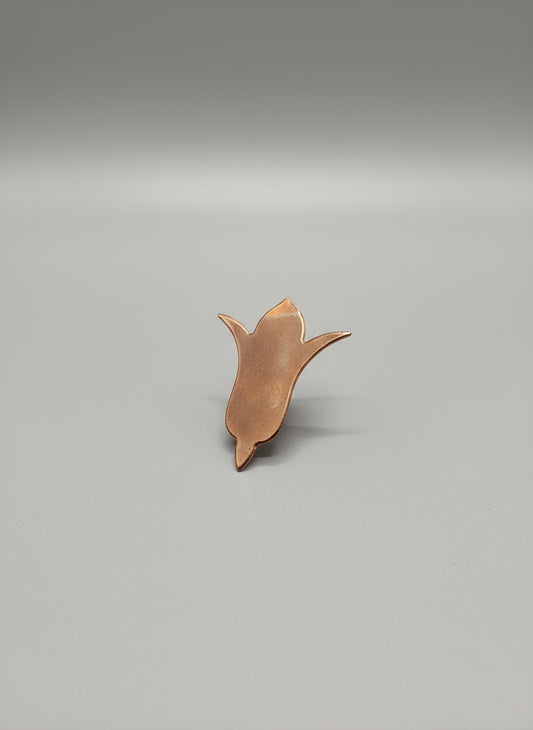 Copper Flower-shaped object on a black cutting mat with grid lines.