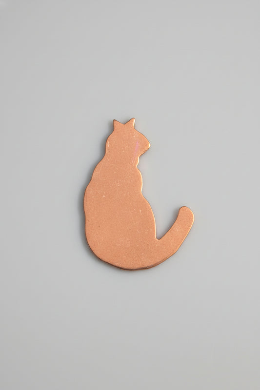Copper cat-shaped object on a black surface with measurement markings