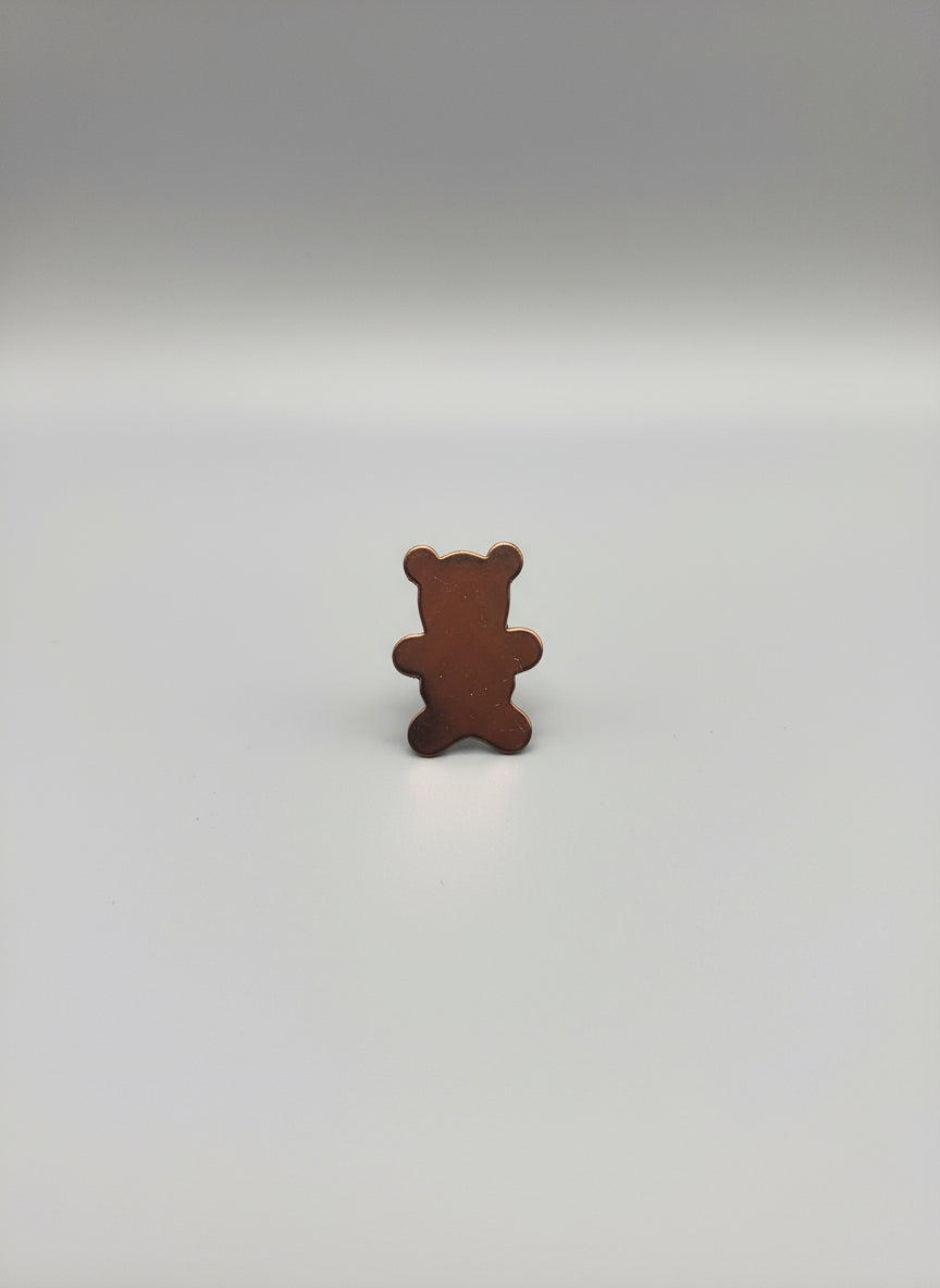 Copper bear-shaped object on a black cutting mat with grid lines.