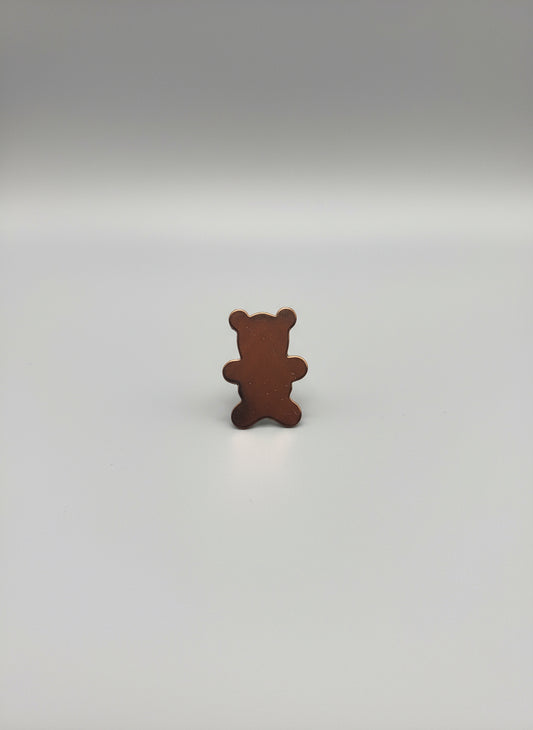Copper bear-shaped object on a black cutting mat with grid lines.