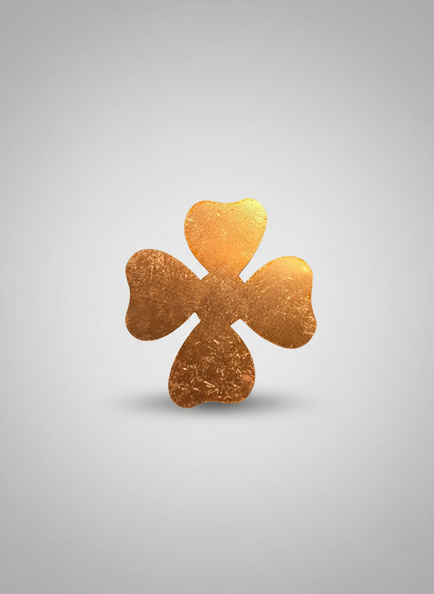 Copper four-leaf clover-shaped object on a black cutting mat with measurement grid.