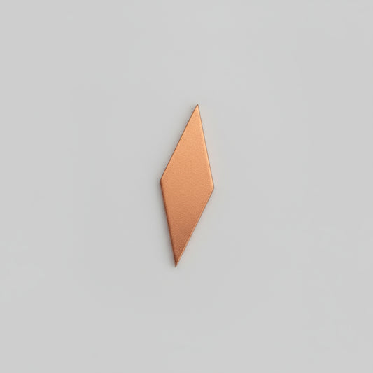 A small, copper blank placed on a black background with measurement markings.