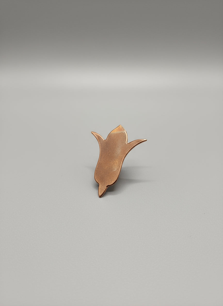 Copper Flower-shaped object on a black cutting mat with grid lines.