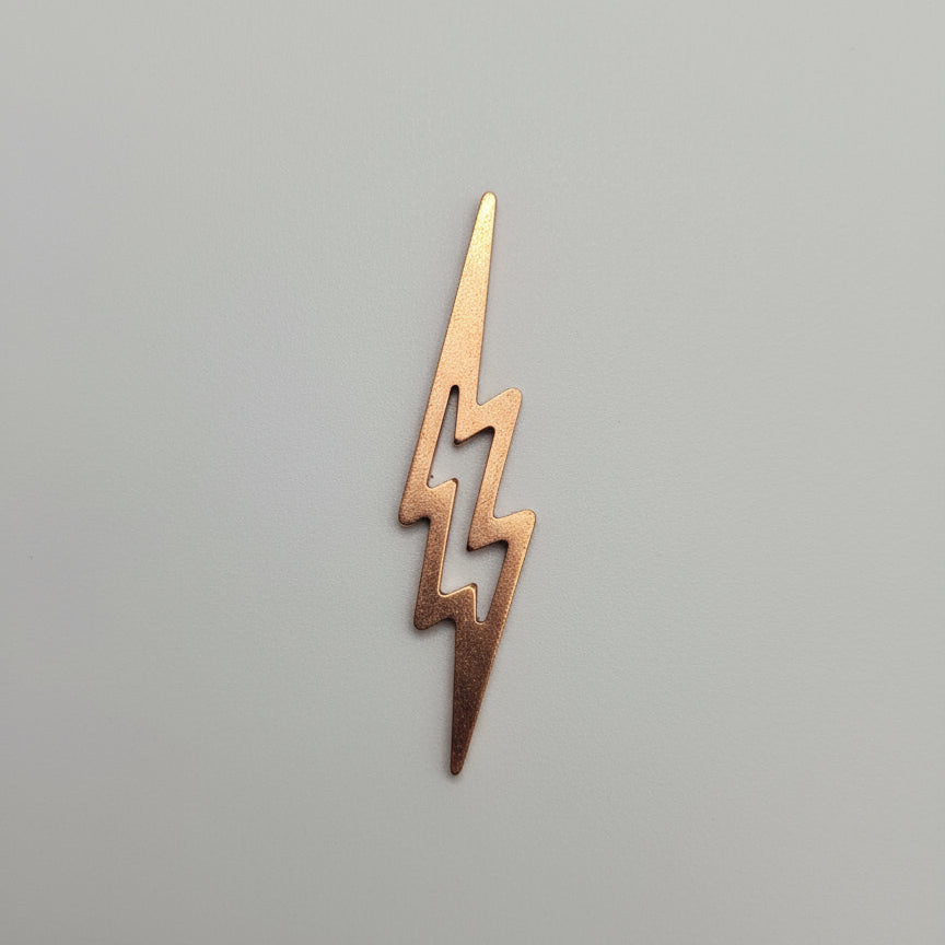 Small copper lightning bolt-shaped object on a black surface with measurement markings.