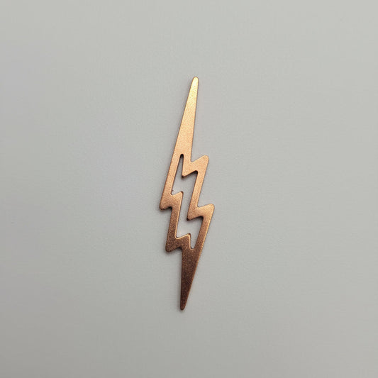 Small copper lightning bolt-shaped object on a black surface with measurement markings.