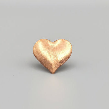 Copper heart-shaped object on a ruler for scale