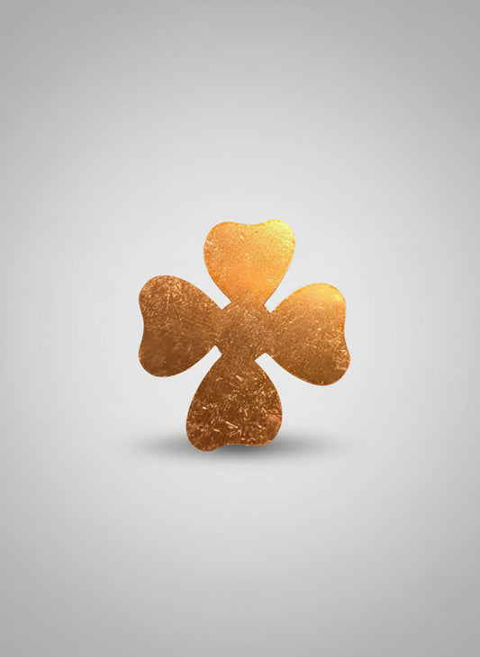 Copper four-leaf clover-shaped object on a black cutting mat with measurement grid.