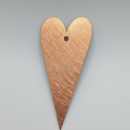 Copper heart-shaped pendant on a black background with measurement scale