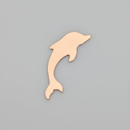 Copper  dolphin-shaped object on a ruler for scale